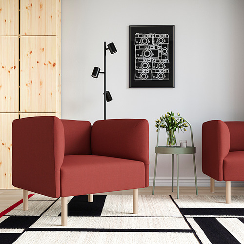 Un sofá LILLEHEM rojo con dos sillas, una mesa auxiliar verde, una lámpara de pared negra y una alfombra multicolor contra una pared clara. Ambiente contemporáneo y acogedor.