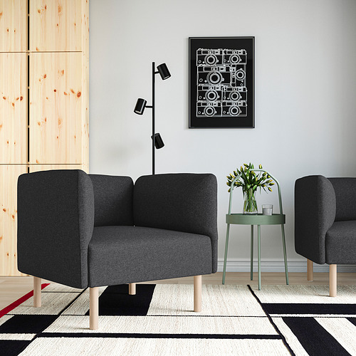Moderno salón con sofá gris LILLEHEM, póster negro, lámpara negra y mesa redonda verde con flores. Alfombra gris debajo.