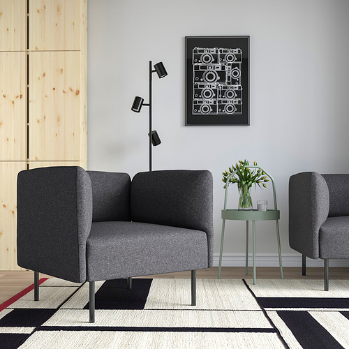Moderno salón con sofá de tela gris LILLEHEM, mesita verde y alfombra geométrica. La impresión artística cuelga por encima.