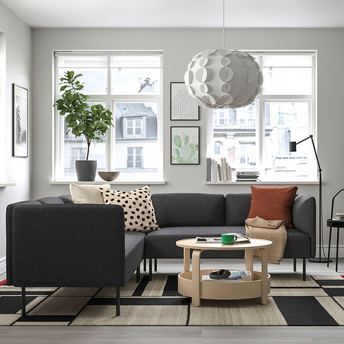 Sala de estar moderna con un gran sofá modular gris LILLEHEM, mesa de centro de madera, alfombra estampada y grandes ventanales que ofrecen una vista urbana.