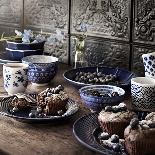 Vajilla azul y blanca con bayas, muffins, café y arte metálico.