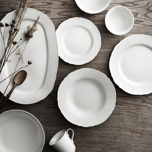 Platos de porcelana blanca, incluyendo platos y tazas, dispuestos sobre mesa de madera.