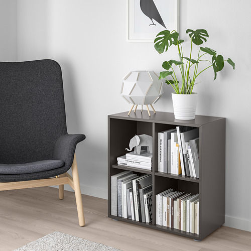 Mueble EKET gris oscuro con libros y planta, junto a una silla gris sobre suelo de madera clara.
