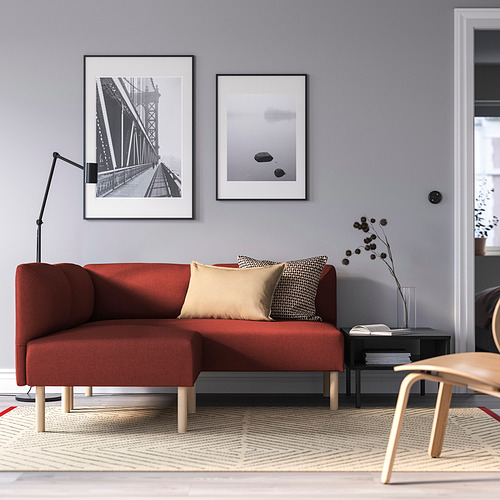 Sala de estar moderna con sofá modular LILLEHEM rojo, arte en blanco y negro, mesa auxiliar, lámpara y silla de madera. Paredes grises y alfombra estampada.