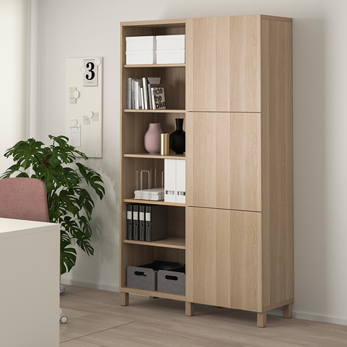 Mueble BESTÅ en madera clara con almacenamiento abierto y cerrado, que muestra la decoración junto a una planta y una pared blanca.