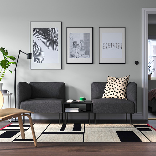 Sala de estar minimalista con sofá LILLEHEM gris oscuro, arte en blanco y negro, alfombra estampada y taza verde sobre una mesa pequeña.