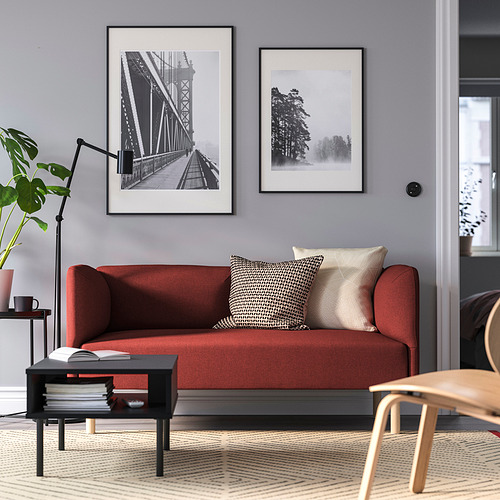 Sala de estar moderna: sofá rojo con almohadas estampadas, mesa de centro con libros, dos grandes fotos enmarcadas, pared gris y gran ventana.
