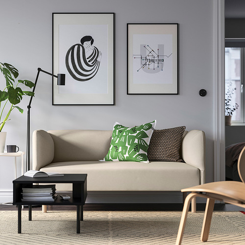Sala de estar moderna con sofá beige, almohadas verdes, arte abstracto, planta, libros, silla.
