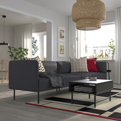 Sala de estar moderna con sofá LILLEHEM, cojines, mesa de centro, gran ventanal, luz de mimbre, alfombra a rayas y decoración de pared.