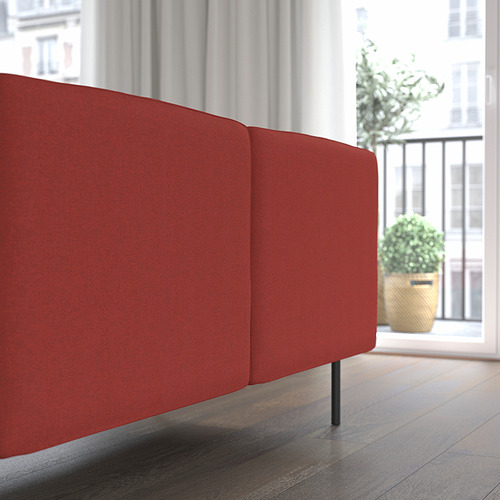 Sofá modular rojo con tela afelpada, colocado cerca de un gran ventanal con plantas en el exterior.