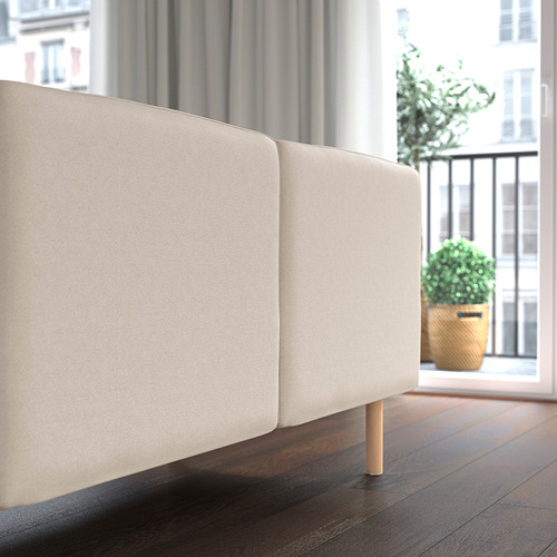 Moderno sofá beige con patas de madera junto a un gran ventanal, mostrando su diseño cómodo y adaptable.