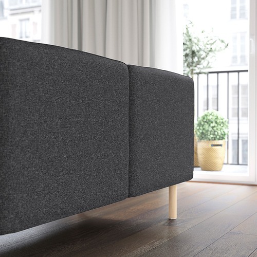 Sofá modular gris oscuro con patas de madera, colocado cerca de una ventana con una planta en maceta. El sofá está diseñado para la personalización y la fácil limpieza.