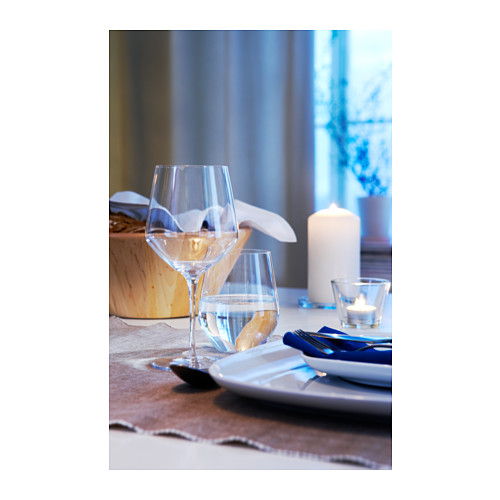 Copa de vino transparente sobre la mesa con vela, servilleta y plato. Diseño sencillo y elegante.