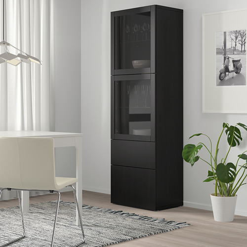 Mueble de cristal negro BESTÅ entre silla y mesa con planta.