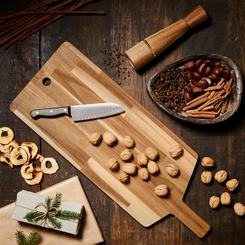 Tabla de cortar SMÅÄTA de madera con cuchillo, nueces y cuenco de especias y frutas sobre una mesa.