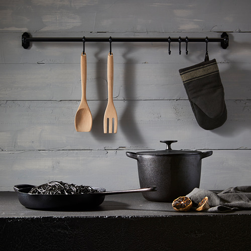 Los utensilios de cocina cuelgan de la barra; mostrador con fideos, naranjas. Pared envejecida. Esta versión conserva los elementos principales a la vez que es concisa.
