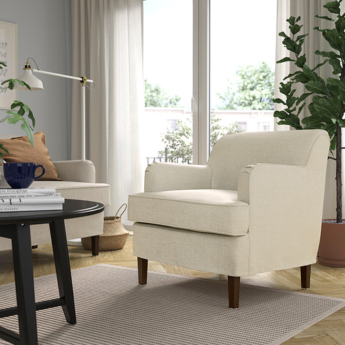 Habitación con 2 sillones ROCKSJÖN beige, uno cerca de la ventana, otro junto a la mesa. La mesa tiene libros, taza y lámpara. Alfombra debajo. Vista al balcón exterior.
