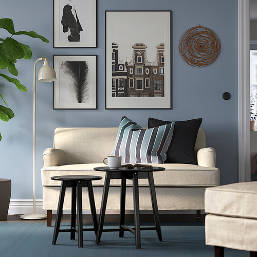Acogedora sala de estar con sofá beige, almohadas oscuras, pared azul, arte, lámpara, planta.