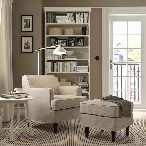Rincón limpio y acogedor con sillón ROCKSJÖN beige, otomana a juego y estantería. El sillón es compacto pero cómodo con tela kilanda.
