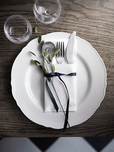 Plato rústico: plato UPPLAGA, servilleta negra, vegetación, cubiertos, vidrio.