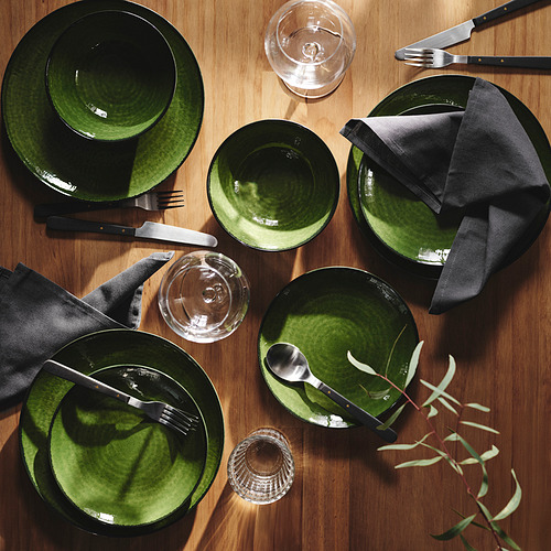 Juego de vajilla, verde oscuro, brillante. Platos, cuencos, vasos, cubiertos dispuestos sobre mesa de madera.