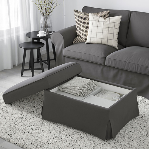 Descripción de la imagen: sala de estar con sofá EKTORP gris y otomana. La otomana tiene un asiento elevable que revela el espacio de almacenamiento con una manta y un libro en el interior.