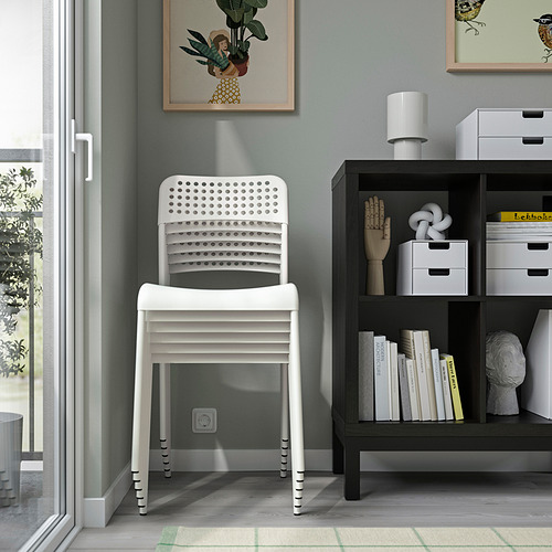 Silla blanca apilable junto a estantes de almacenamiento y ventanas, que ilustra el uso en interiores.