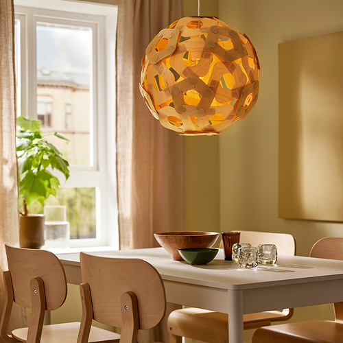 Comedor moderno con una gran lámpara colgante geométrica de color naranja, sillas de madera y mesa con cuencos y tazas.