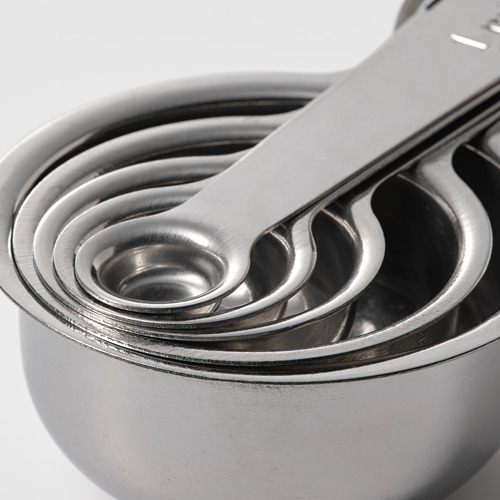 Cinco tazas medidoras de acero inoxidable apiladas, pulidas y relucientes, anidadas cuidadosamente para un almacenamiento compacto.