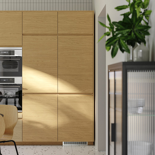 Cocina moderna con gabinetes de roble VOXTORP, manijas elegantes, electrodomésticos integrados y planta verde.