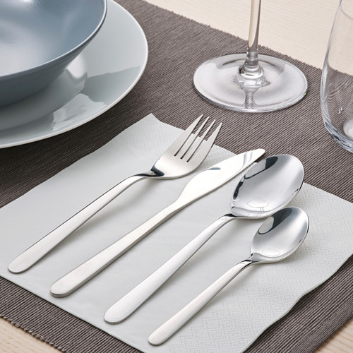 Cubiertos de plata colocados en una servilleta blanca, que incluyen tenedor, cuchillo y cuchara, dispuestos cuidadosamente sobre una mesa de comedor con copas de vino.