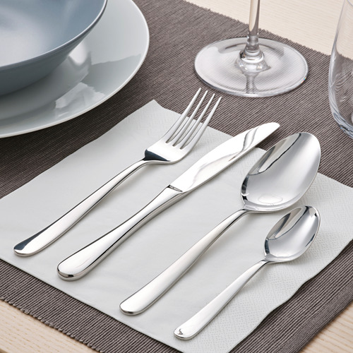 Un juego de cubiertos de acero inoxidable cuidadosamente dispuestos en un mantel individual, que incluye un tenedor, un cuchillo, una cuchara y una cucharadita. Parte de un juego de comedor de 30 piezas.