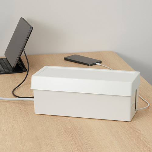 La caja SÄTTING blanca organiza los cables del escritorio en un escritorio de madera.