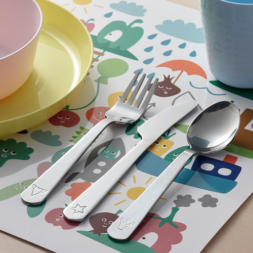 Cubiertos infantiles colocados sobre colchoneta de colores. Incluye tenedor, cuchara y cuchillo con filo dentado, perfecto para manos pequeñas.