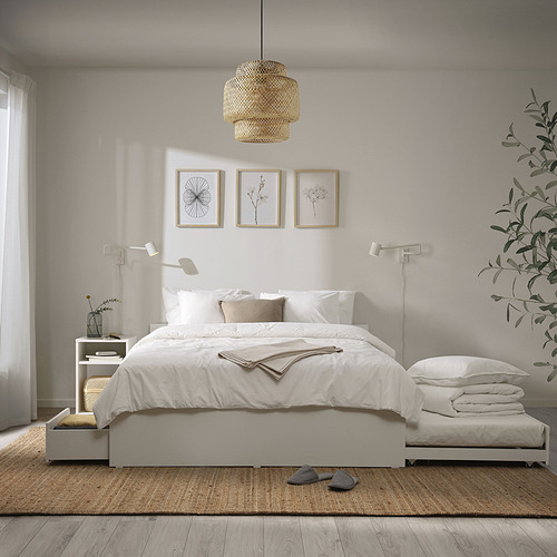 Dormitorio minimalista con cama y almacenamiento VIHALS, sábanas blancas, almohada beige, lámparas colgantes y de pared, plantas, zapatillas. Alfombra neutra, suelo de madera.