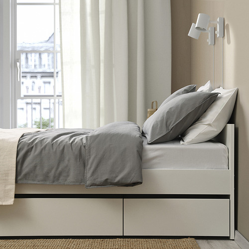 Cama moderna con sábanas grises, almacenamiento debajo, lámpara de pie, vista a la ciudad.