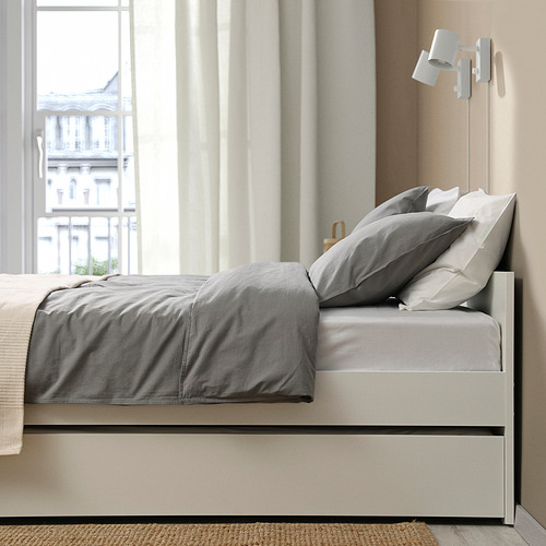 Una cama moderna con sábanas grises y almacenamiento nido, con luces montadas en la pared.