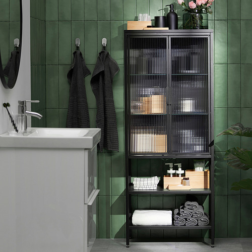 Baño con azulejos de color verde oscuro con gabinete de musgo, toallas y plantas.