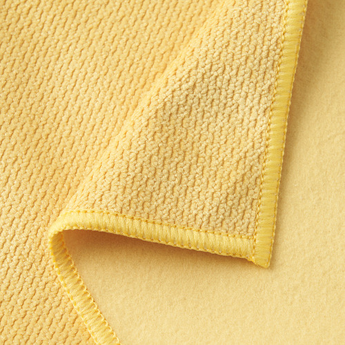Primer plano de un paño de microfibra amarillo suave que resalta su superficie texturizada y las costuras amarillas en el dobladillo, que muestran su calidad.