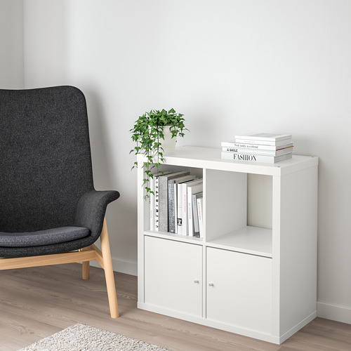 Sala de estar minimalista con almacenamiento KALLAX y silla oscura. KALLAX sostiene libros y una planta.