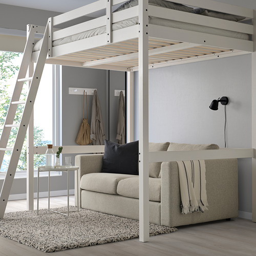 Una cama alta STORÅ blanca con una escalera a la izquierda, más grande que los muebles circundantes, con un sofá debajo.
