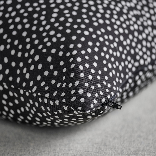 Funda de cojín negra con patrón de puntos blancos, detalle de cremallera, colocada sobre una superficie gris claro.
