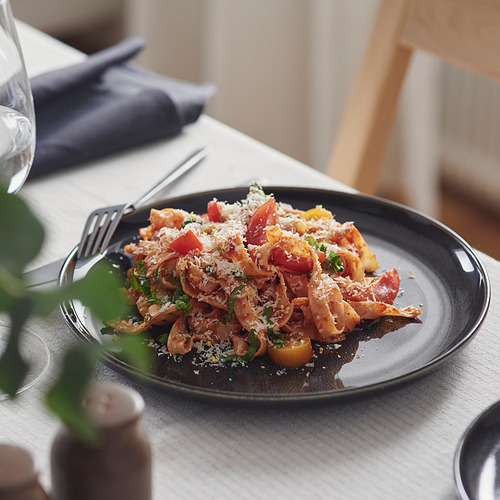 Plato de pasta con tomates cherry y queso rallado en un plato oscuro con tenedor, colocado en la mesa del comedor.