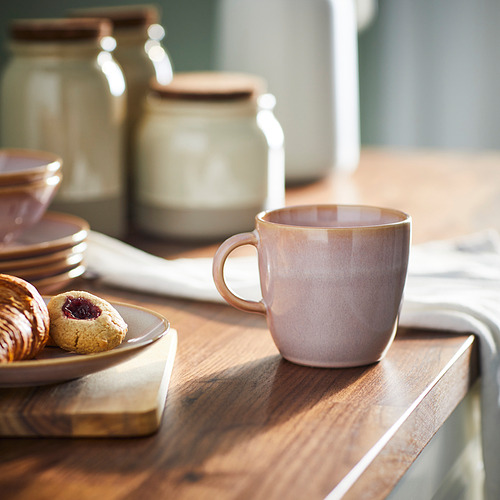 Taza FÄRGKLAR sobre mesa de madera, junto a pasteles, jarras y platos. Color rústico, diseño sencillo, material de gres, tamaño mediano.
