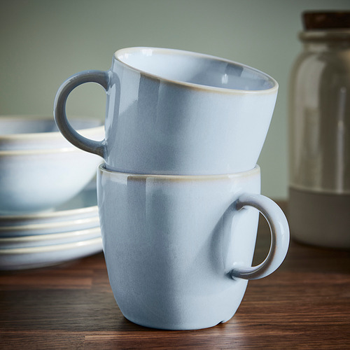 Dos tazas de color azul claro apiladas sobre una mesa de madera, que muestran su diseño sencillo y funcional y su exclusivo acabado esmaltado.