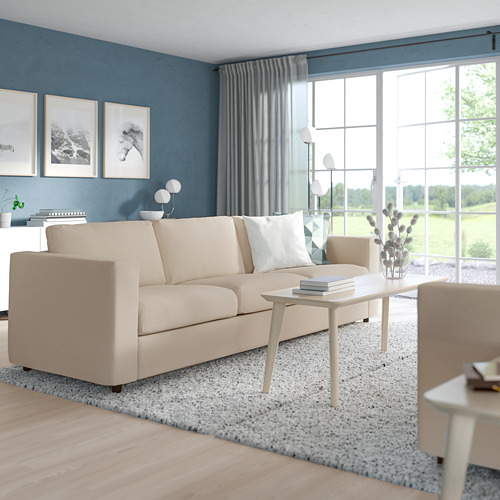Sala de estar moderna con sofá VIMLE beige, combina con la decoración neutra, incluida la alfombra moteada. Los grandes ventanales llevan la naturaleza al interior.