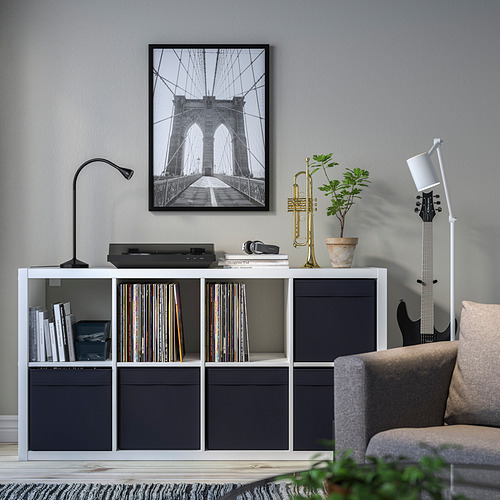 Sala de estar moderna con almacenamiento DRÖNA, vinilos, libros, trompeta, planta, lámpara, guitarra y foto del puente de Brooklyn.