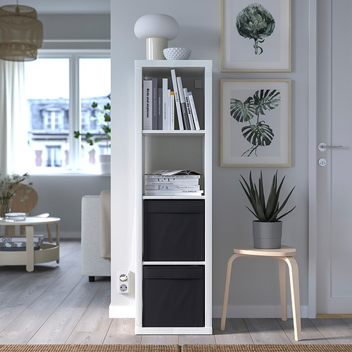 Salón moderno con estanterías kallax, cajas DRÖNA, lámpara y decoración. Taburete de madera con plantas, estampados artísticos y acogedora alfombra junto a grandes ventanales.