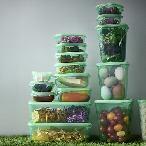 Recipientes de plástico transparente y verde para alimentos, apilados con verduras y frutas, que muestran el almacenamiento organizado en el refrigerador.