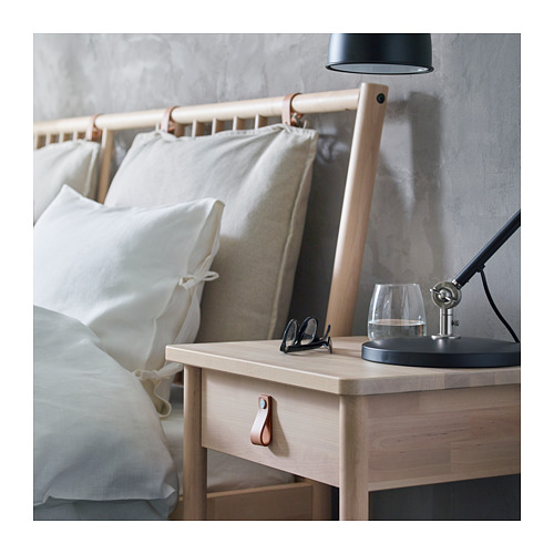 Mesita de noche minimalista de madera clara con lámpara negra, cristal y tijeras.